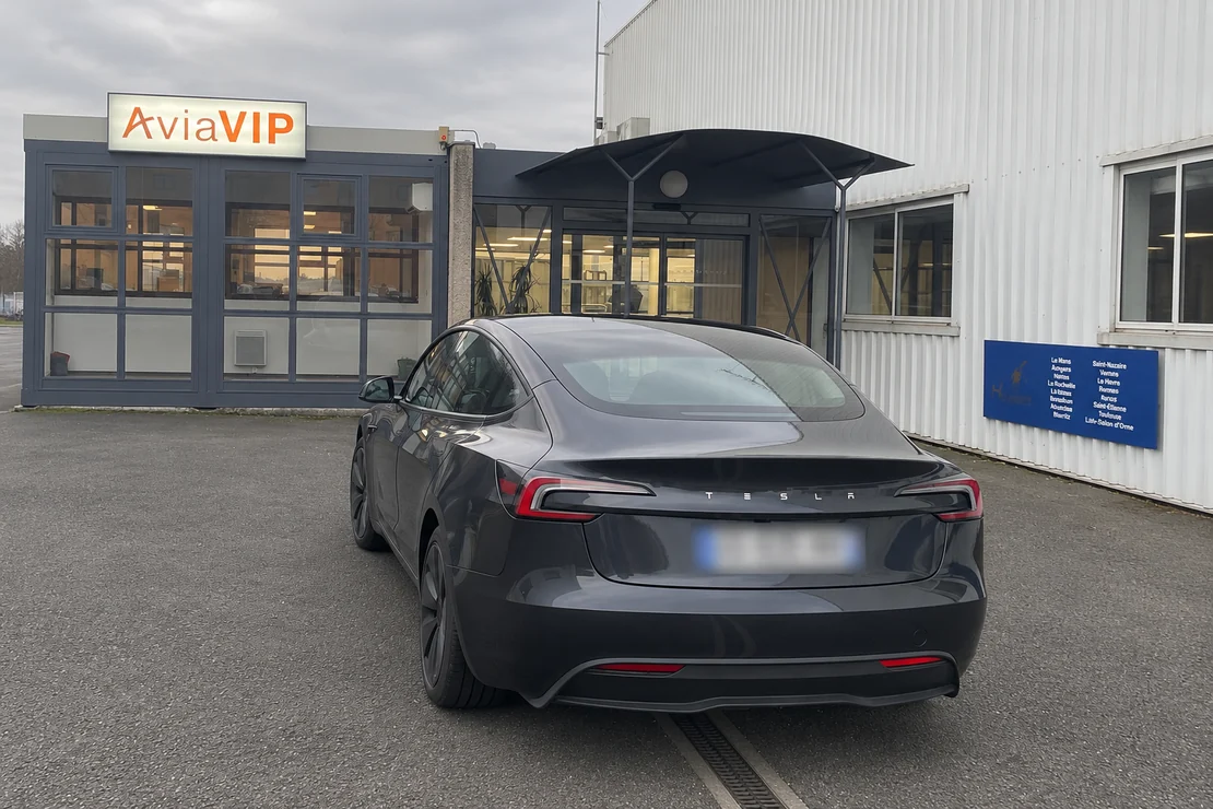 Tesla Model 3 graphite stationnée devant une entrée portant l’enseigne AviaVIP.