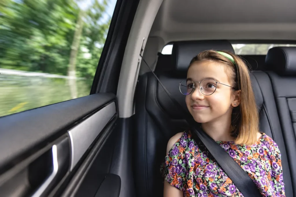 Une enfant portant des lunettes est assise à l’arrière d’une voiture, ceinture attachée.