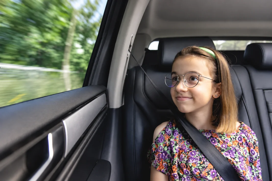 Une enfant portant des lunettes est assise à l’arrière d’une voiture, ceinture attachée.